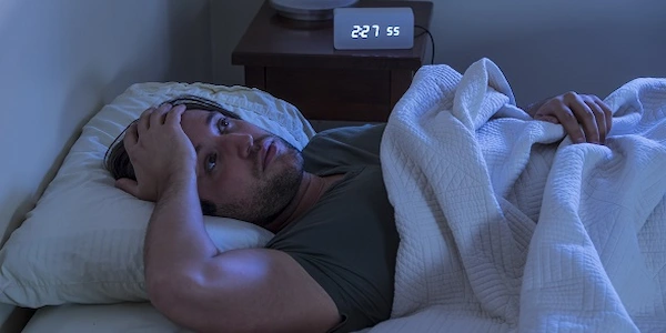 Man staring at ceiling in dark bedroom - sleepless night - frustration