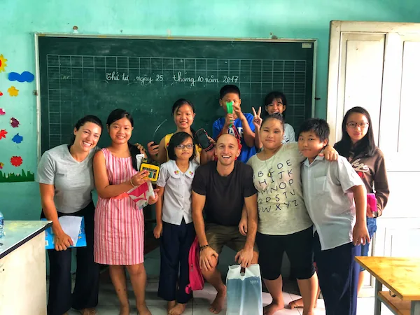 Expat teacher smiling with a group of Vietnamese students in a classroom - expat volunteer teaching - classroom interaction